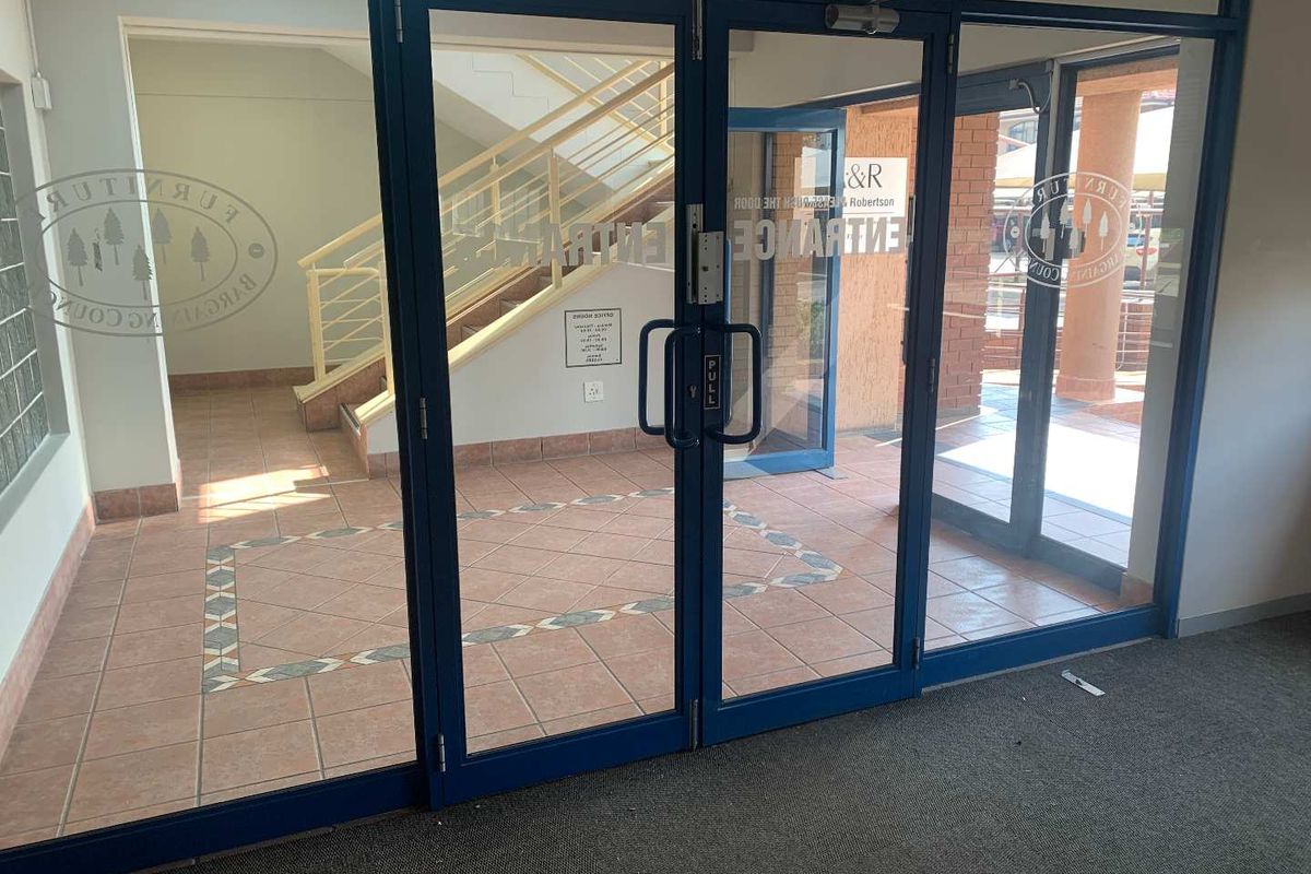 Office building entrance featuring glass double doors, tiled flooring, and an internal staircase leading to upper levels.