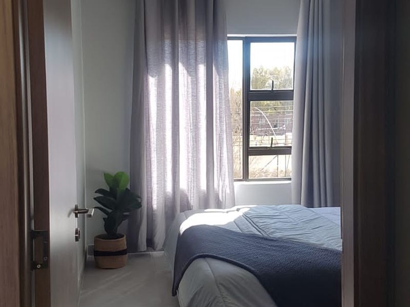 A well-lit bedroom featuring neutral tiled flooring, modern aluminium window frames, and a clean, minimalist aesthetic.