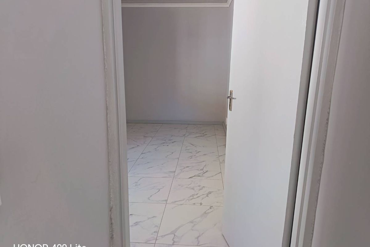 An empty bedroom featuring modern marble-effect floor tiles and a clean panelled ceiling, viewed through an open doorway.