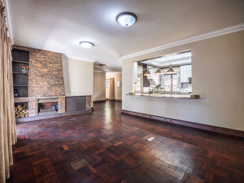 Spacious open-plan living area featuring a stone fireplace, classic parquet flooring, and a convenient breakfast bar pass-through to the kitchen.