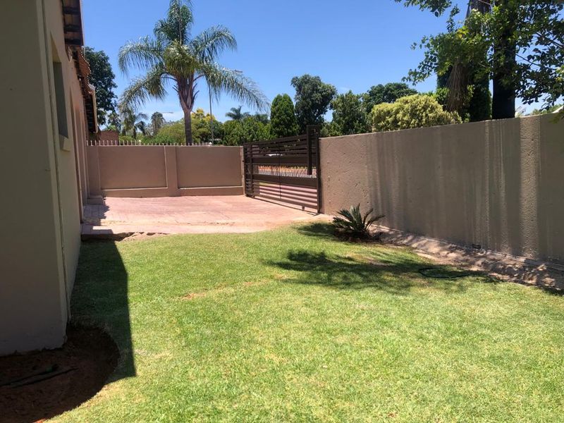 A private rear garden featuring a lawn, paved area, and secure perimeter wall with a metal sliding gate.