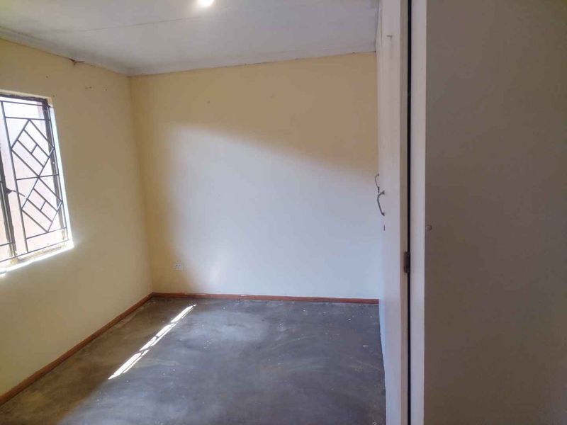 An empty bedroom featuring a window with a security gate and plain wall finishes, ready for renovation or staging.