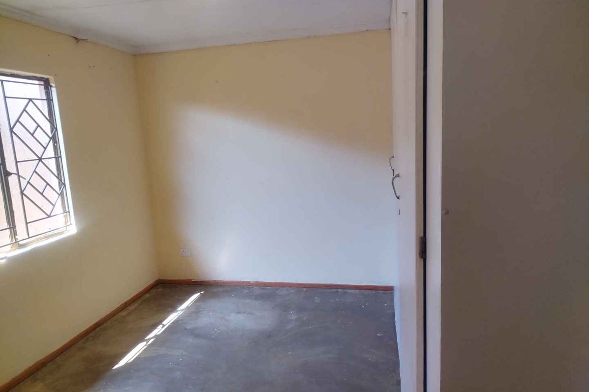 An empty bedroom featuring a window with a security gate and plain wall finishes, ready for renovation or staging.