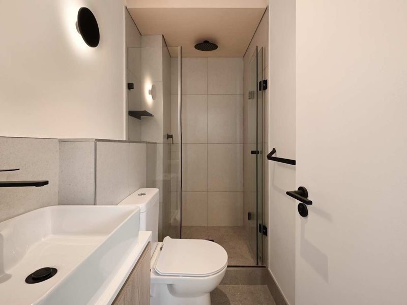 Modern bathroom featuring a walk-in shower with a rain shower head, contemporary vanity basin, and sleek matte black fixtures throughout.