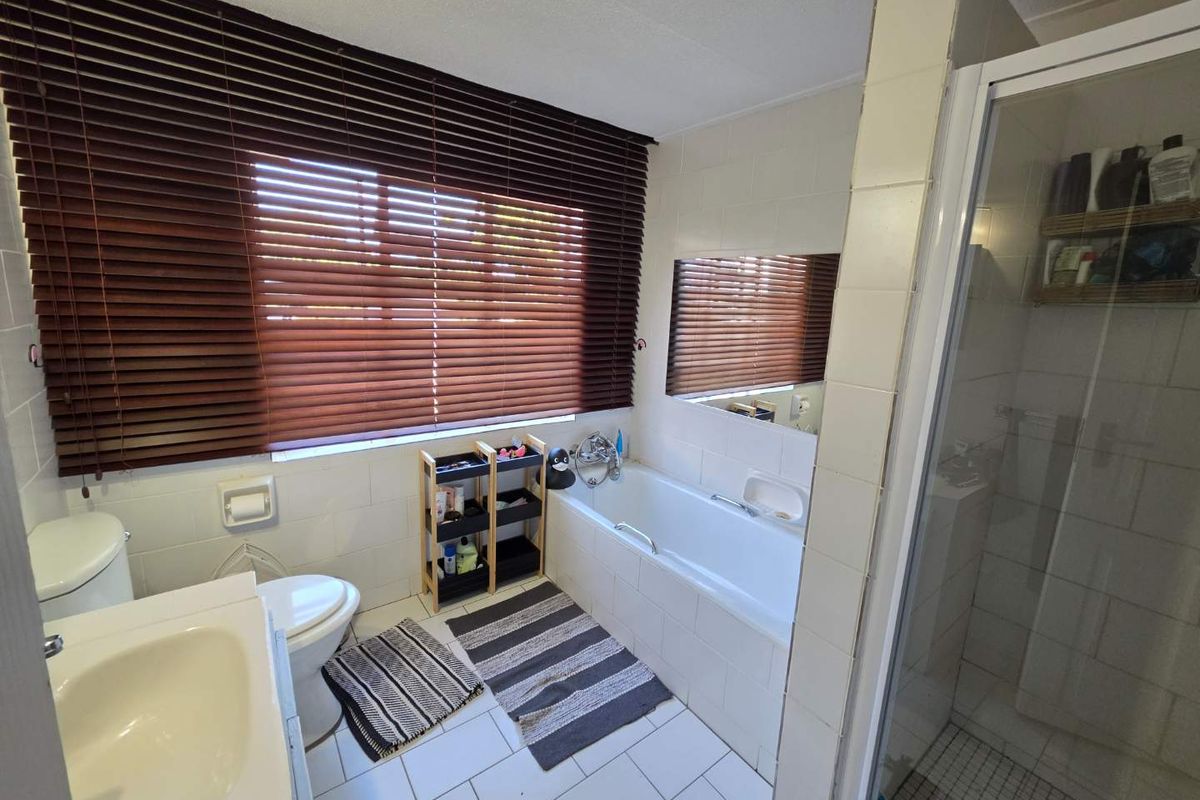 A functional bathroom featuring a built-in bathtub, separate glass-enclosed shower, vanity basin, and toilet with tiled walls and flooring.