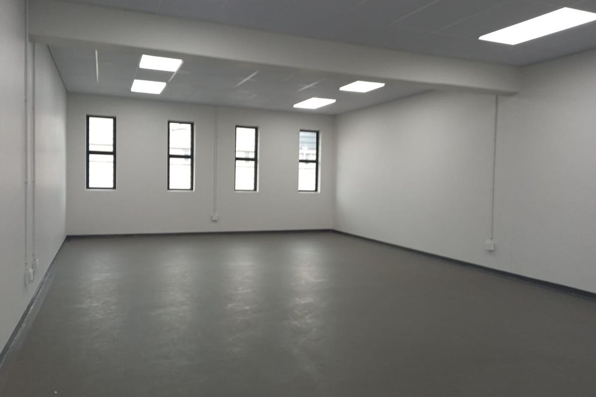 A spacious, empty industrial office area featuring neutral walls, painted concrete flooring, and recessed ceiling lighting, providing a clean and versatile workspace.