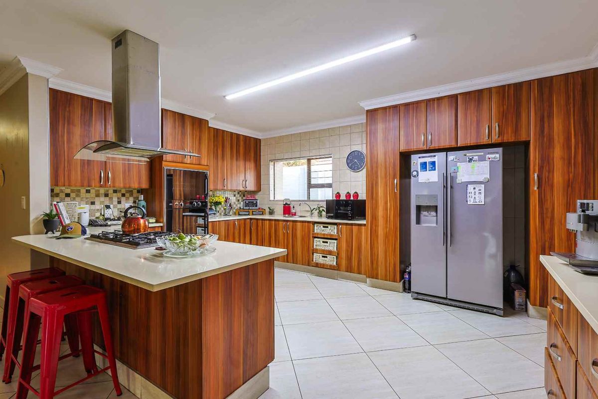 Spacious kitchen featuring wood-grain cabinetry, a central island with a built-in gas hob, stainless steel extractor fan, and tiled flooring.