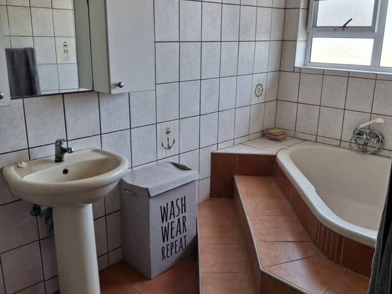 A dated bathroom featuring a pedestal basin, a built-in tiled bathtub with steps, and full-height wall tiling.