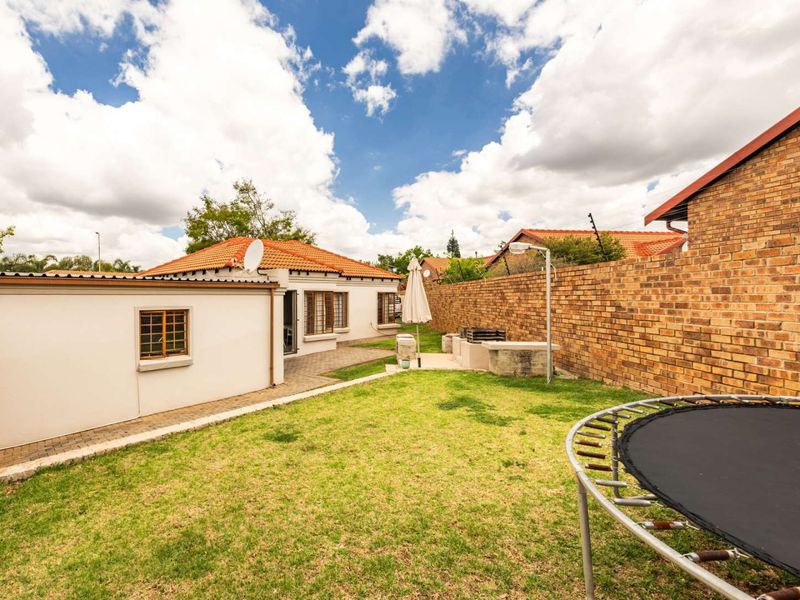 A private rear garden featuring a lawn, paved walkway, and a built-in braai area enclosed by a brick boundary wall.