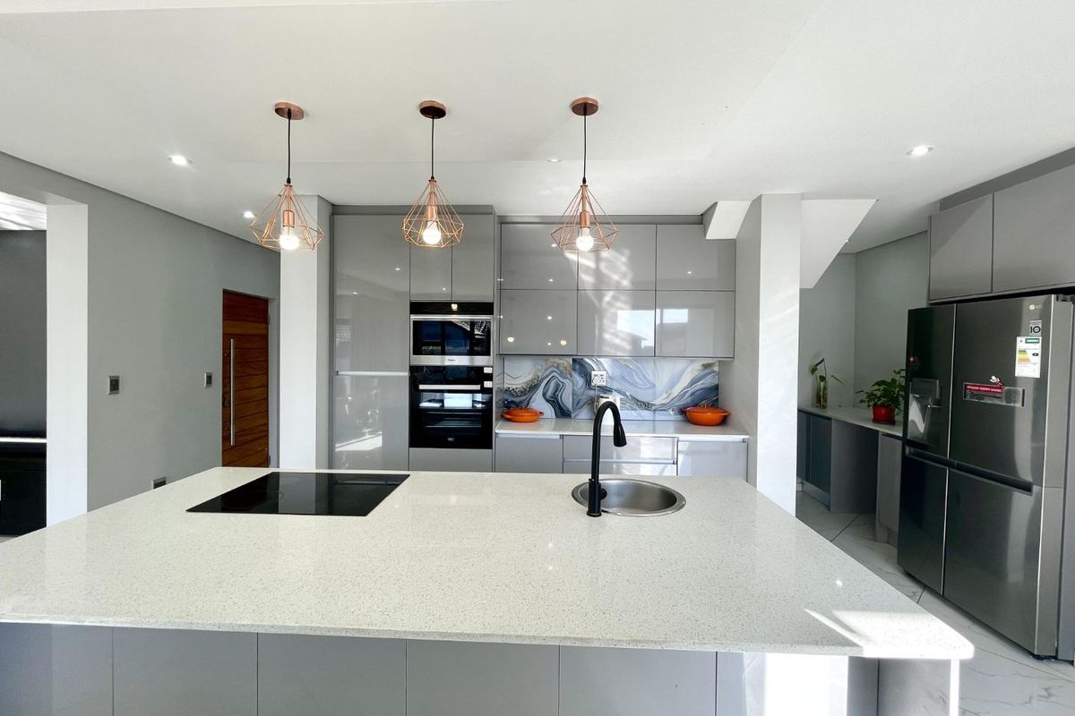 Modern kitchen featuring a central island with quartz countertops, high-gloss cabinetry, built-in appliances, and a stylish feature splashback.
