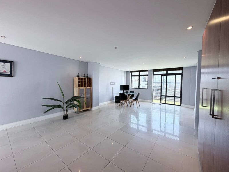 Spacious open-plan living area featuring polished floor tiles, recessed lighting, and large sliding glass doors leading to an outdoor balcony.