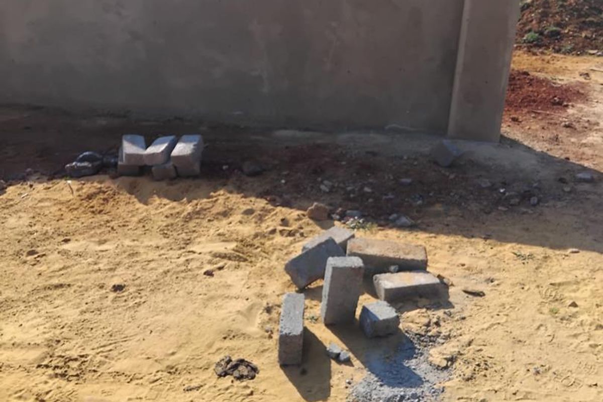 A view of a vacant residential plot featuring a newly constructed plastered perimeter wall and unlandscaped sandy ground.