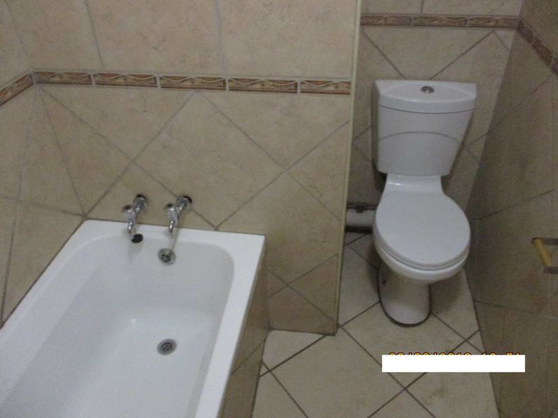 A functional bathroom featuring a standard bathtub and toilet with neutral ceramic wall and floor tiling.