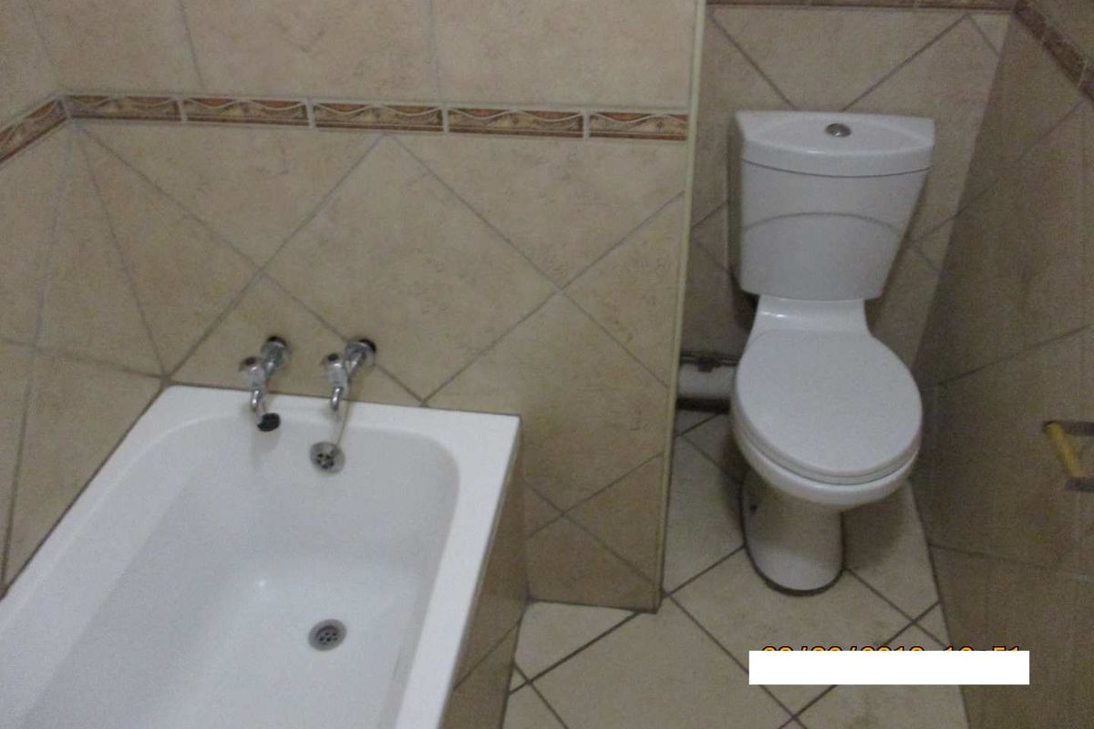 A functional bathroom featuring a standard bathtub and toilet with neutral ceramic wall and floor tiling.