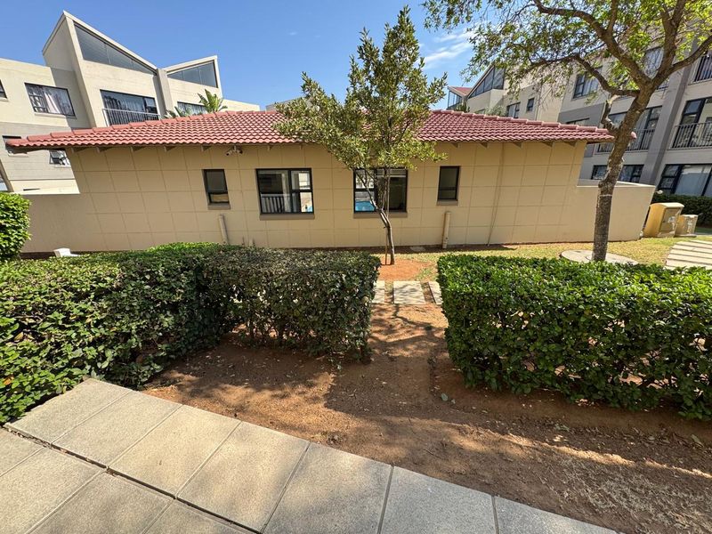 Rear view of the apartment building featuring a tiled roof, external windows, and a landscaped garden area with a paved walkway.