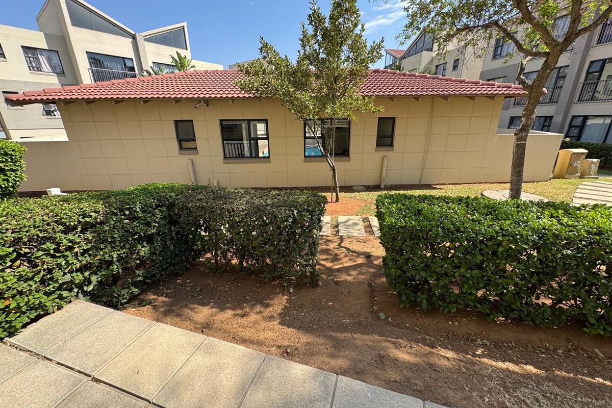 Rear view of the apartment building featuring a tiled roof, external windows, and a landscaped garden area with a paved walkway.