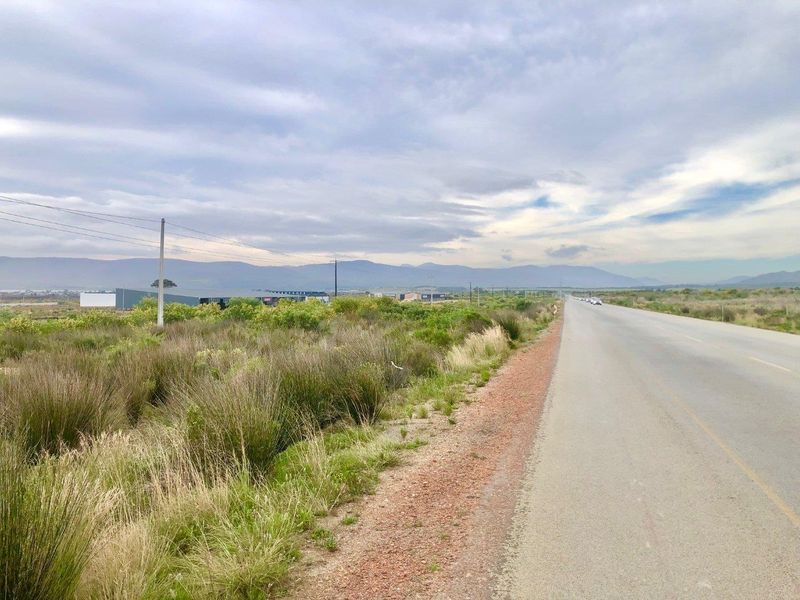 A view of the asphalt road adjacent to the vacant commercial land, featuring surrounding indigenous vegetation and distant mountain views.