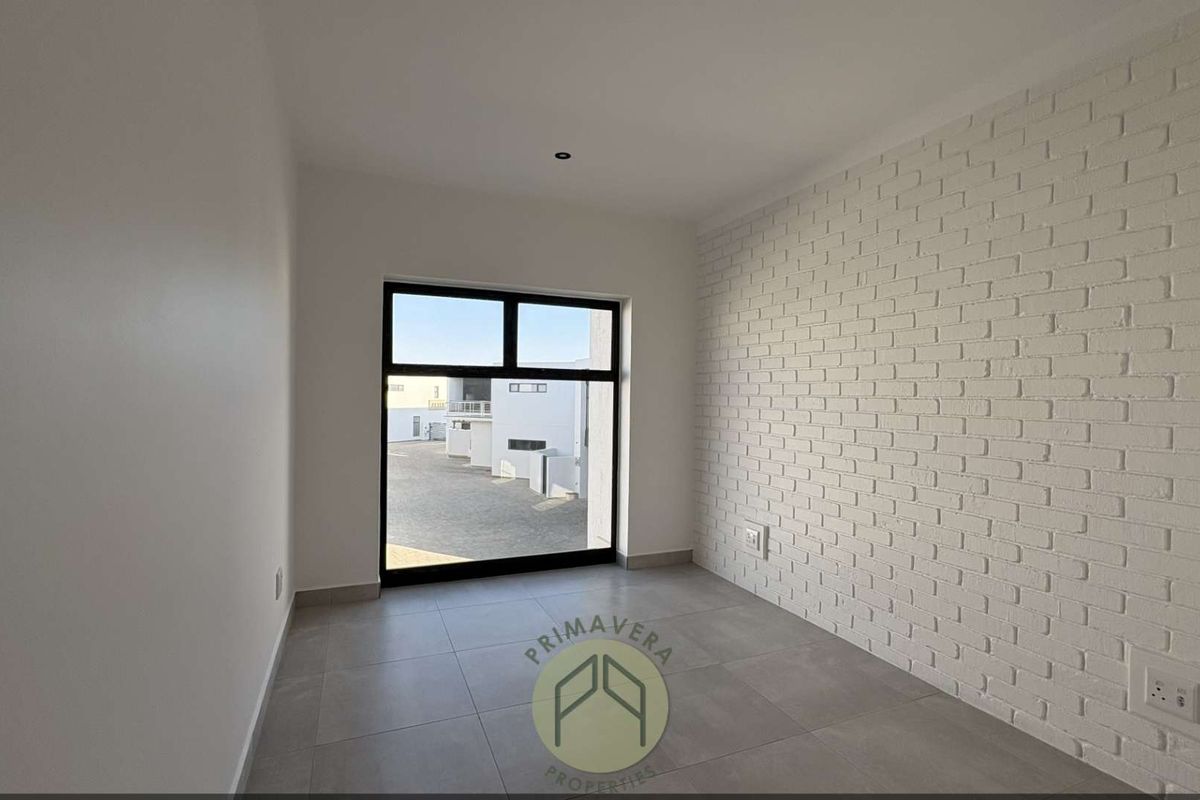 A bright, empty bedroom featuring modern grey floor tiles and a white painted brick feature wall with a large window.