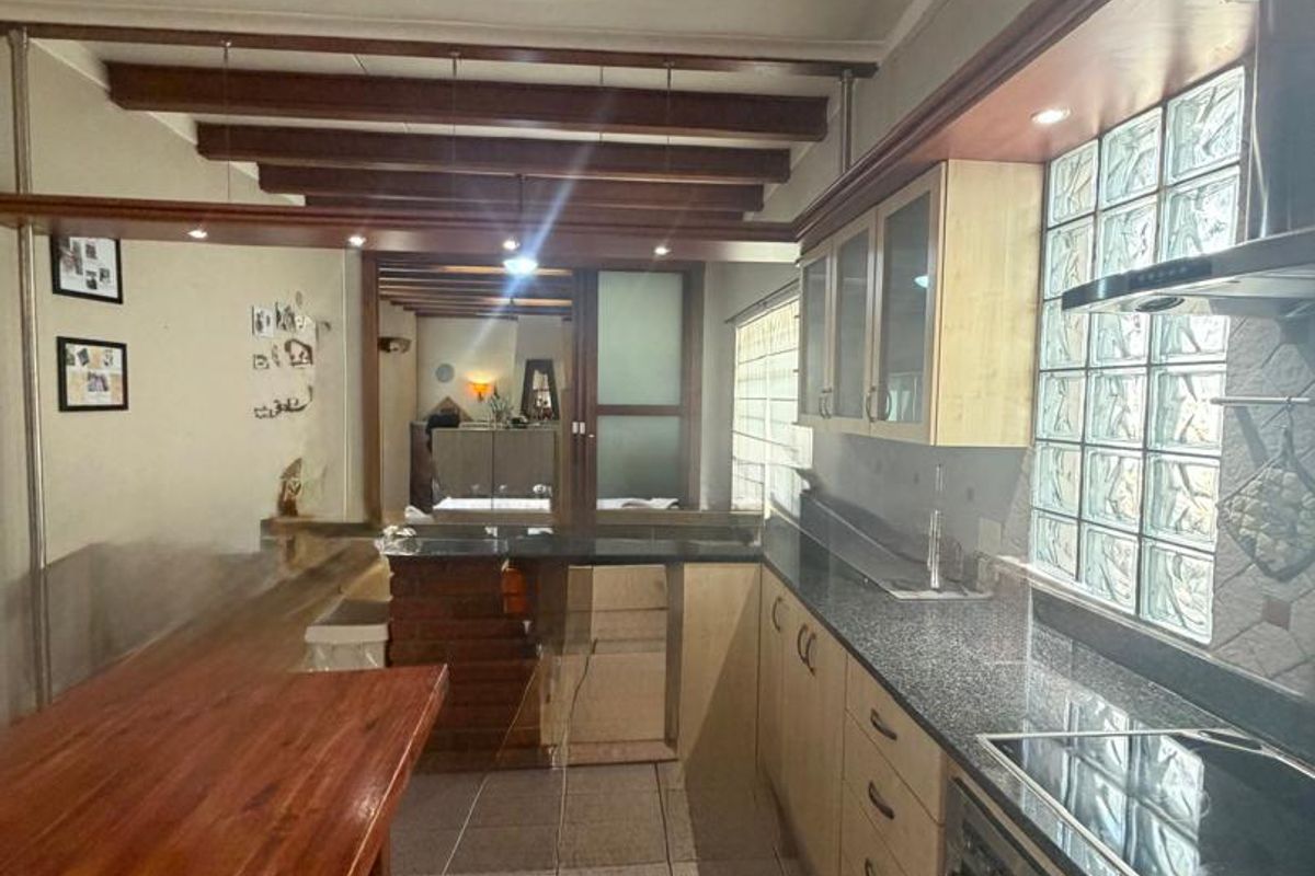 A functional kitchen featuring granite countertops, built-in cabinetry, an electric hob with extractor, and distinctive glass block windows with exposed timber ceiling beams.