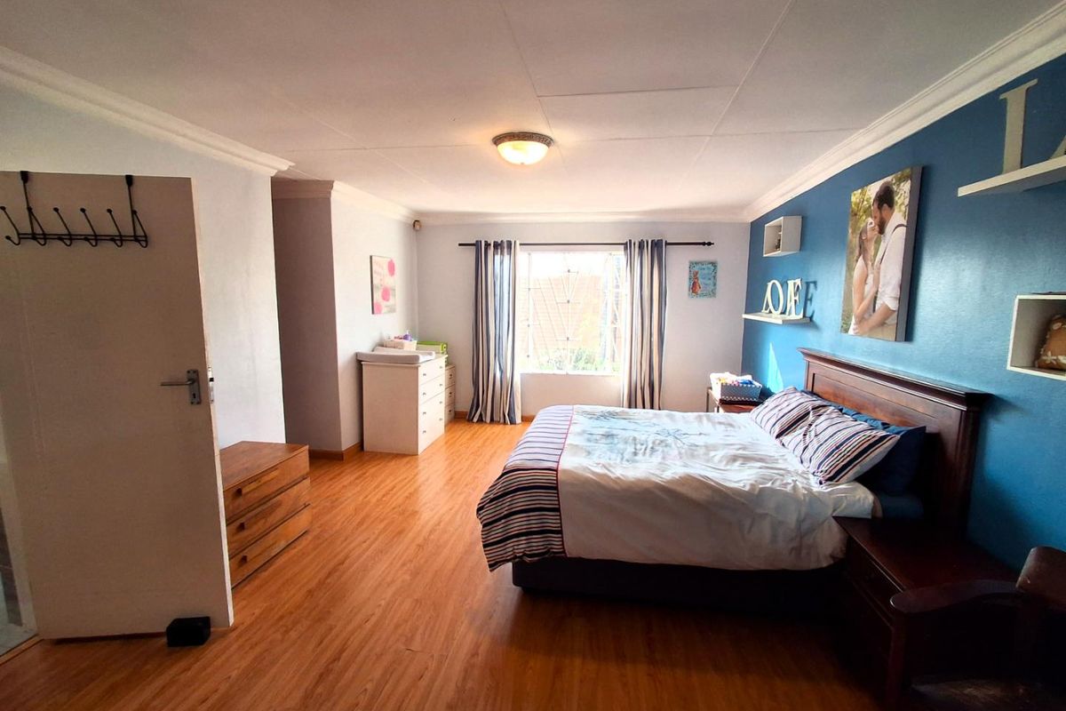 Spacious bedroom featuring laminate flooring, neutral wall tones, and a blue accent wall, providing a comfortable and functional living space.