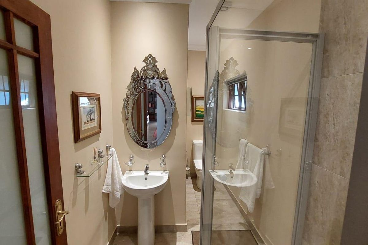 A functional bathroom featuring a pedestal basin, a glass-enclosed shower, and neutral floor and wall tiling.