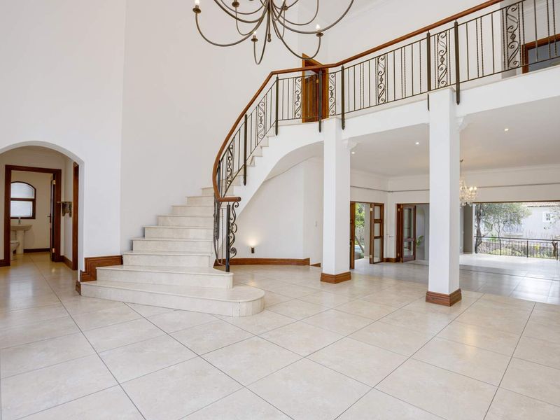 Spacious double-volume entrance hall featuring a grand curved staircase with wrought iron balustrades and elegant tiled flooring throughout.