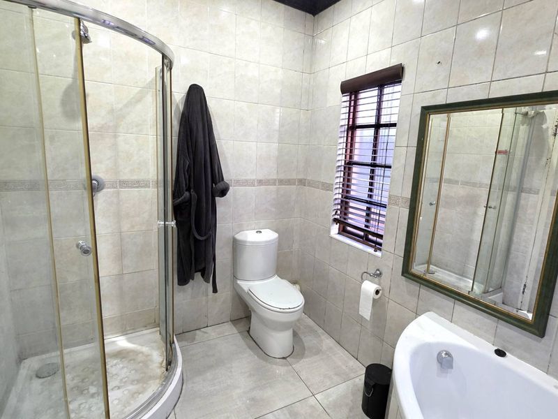 A functional bathroom featuring a corner shower enclosure, a bathtub, a toilet, and full-height wall tiling.