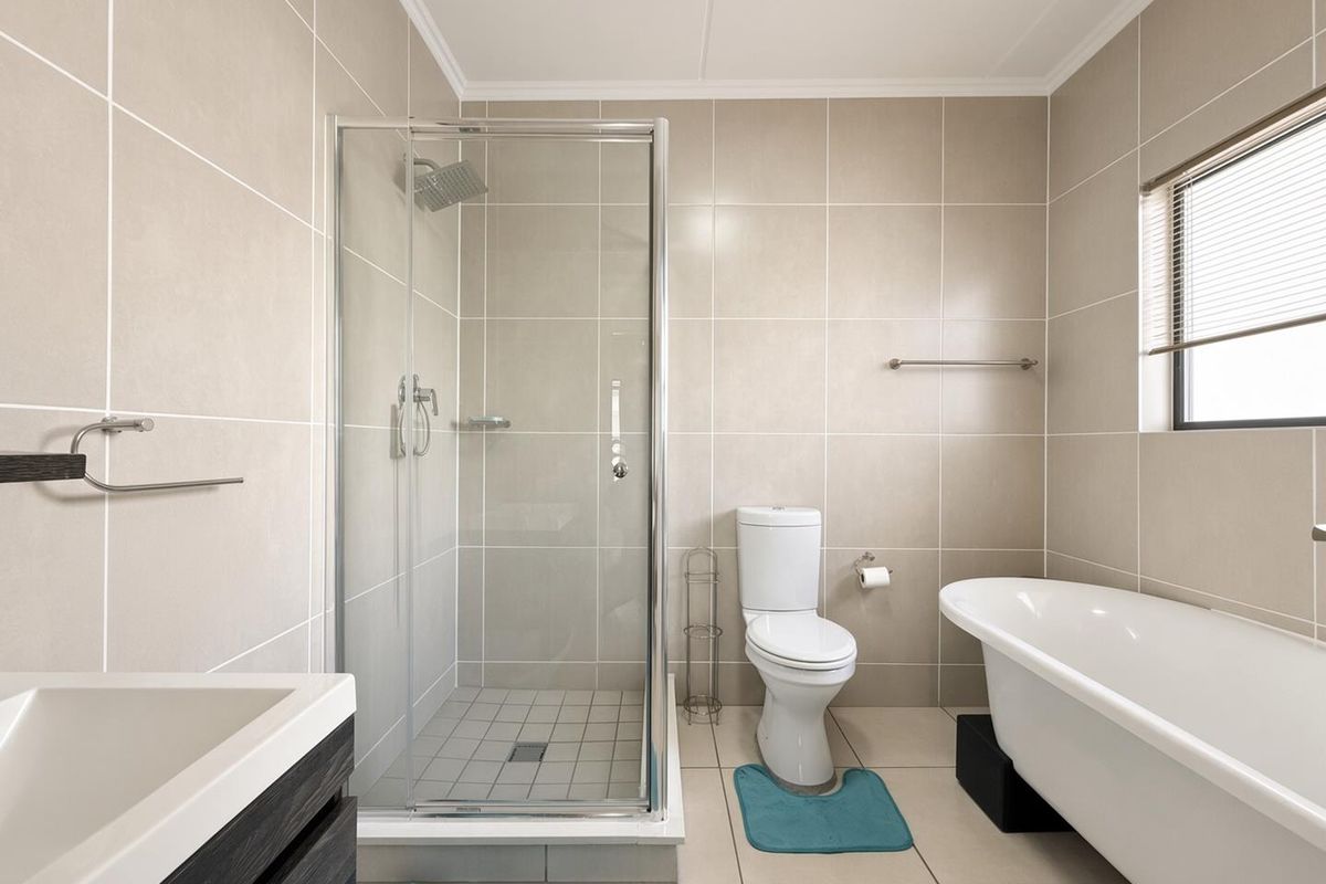 Modern bathroom featuring a glass-enclosed shower, a freestanding bathtub, a vanity cabinet, and neutral floor-to-ceiling wall tiling.