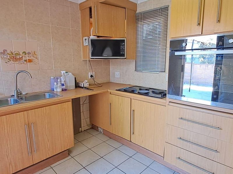 A functional kitchen featuring light wood-look cabinetry, built-in oven and hob, double sink, and tiled splashbacks with neutral ceramic floor tiles.