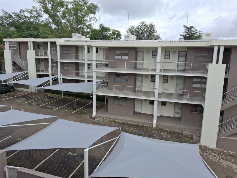 Exterior view of a multi-story apartment complex featuring private balconies, external staircases, and covered parking bays with shade sails.