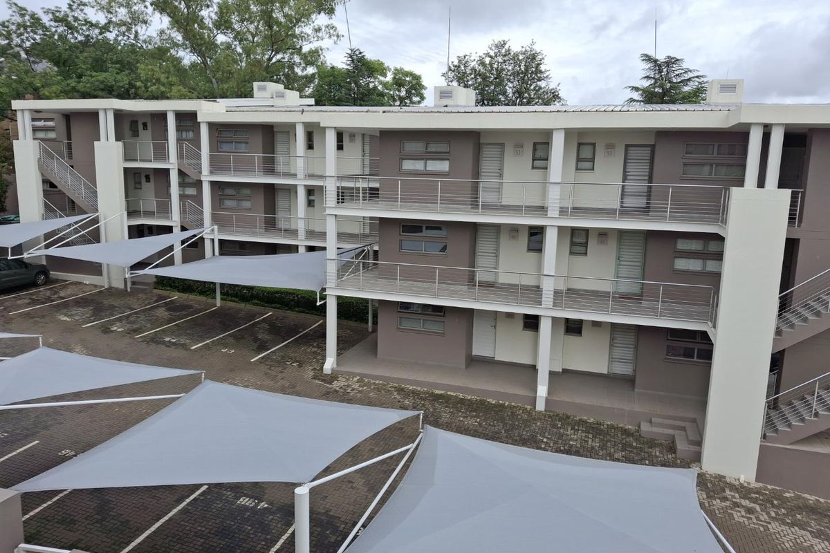 Exterior view of a multi-story apartment complex featuring private balconies, external staircases, and covered parking bays with shade sails.