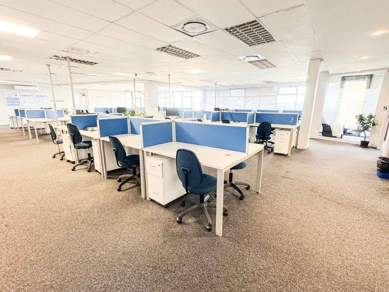 Open-plan office space featuring partitioned workstations, suspended ceilings with recessed lighting, and carpeted flooring.