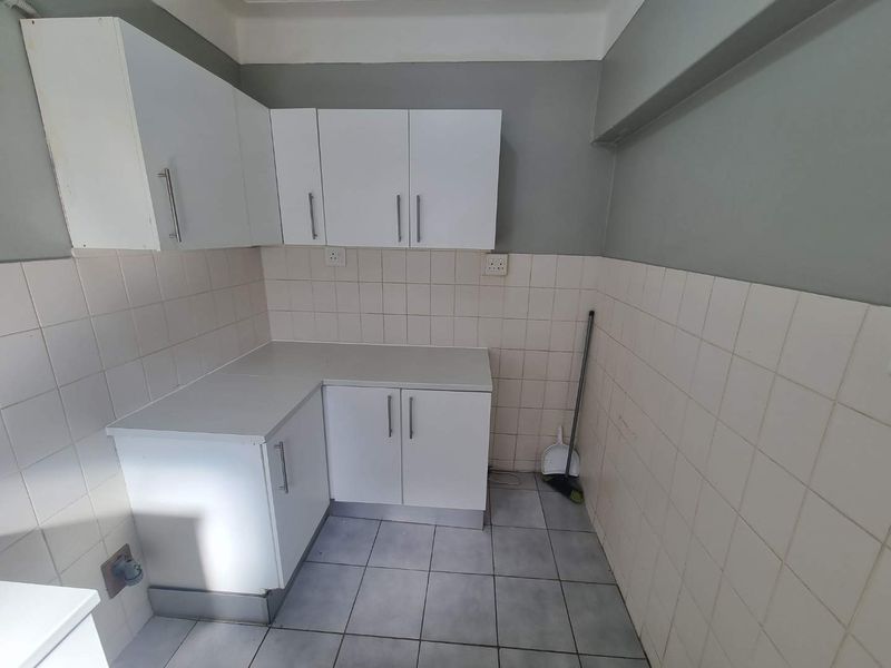 A compact kitchen area featuring white built-in cabinetry, tiled splashbacks, and tiled flooring, offering a functional space ready for updates.