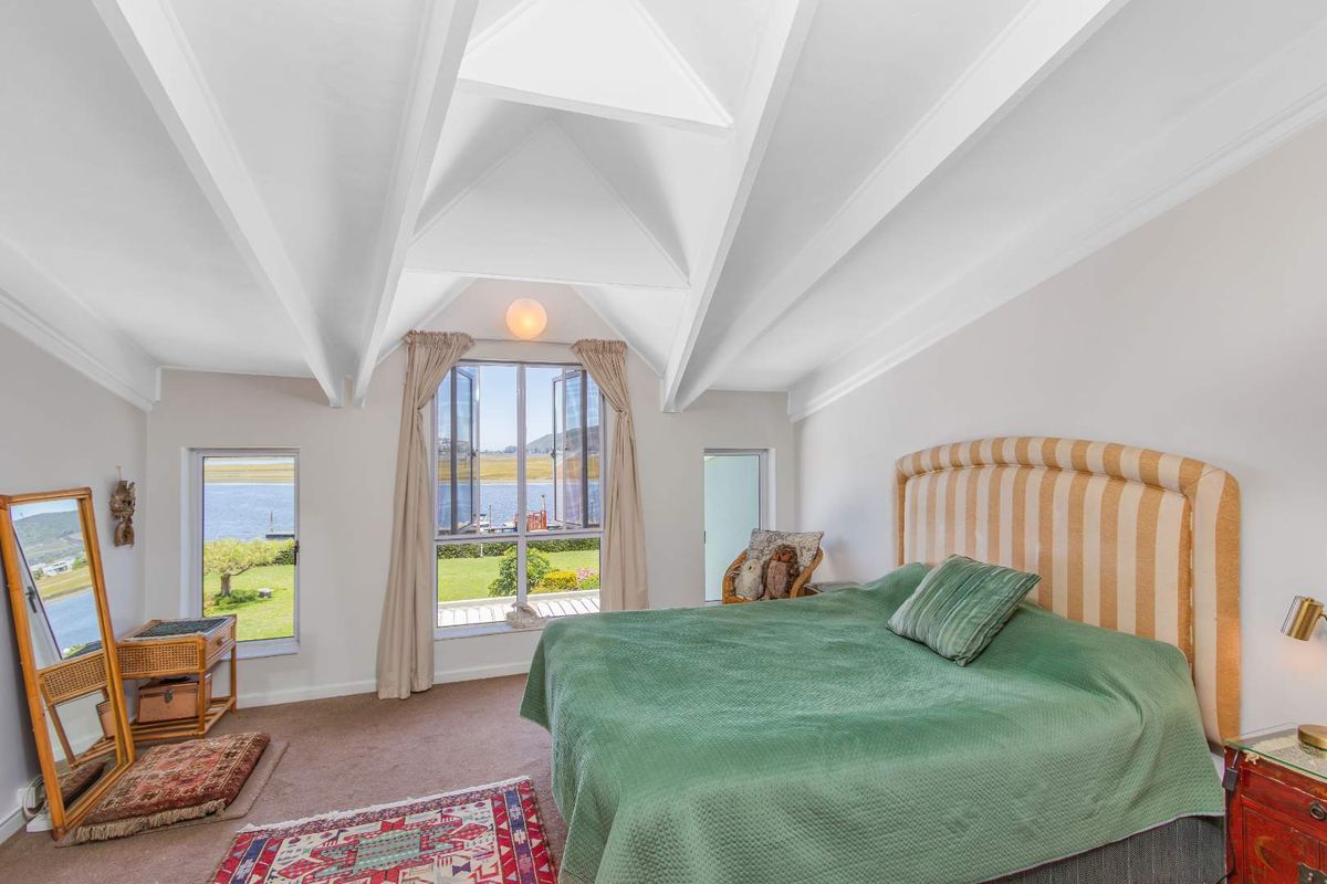 A bright bedroom featuring high vaulted ceilings with exposed beams and large windows offering scenic water views.