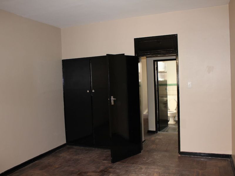 An empty bedroom featuring dark built-in cupboards, parquet flooring, and a doorway leading to an adjacent bathroom.