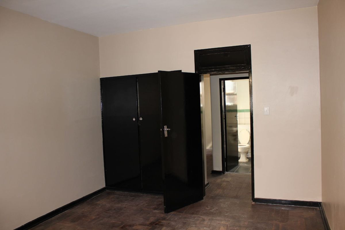 An empty bedroom featuring dark built-in cupboards, parquet flooring, and a doorway leading to an adjacent bathroom.