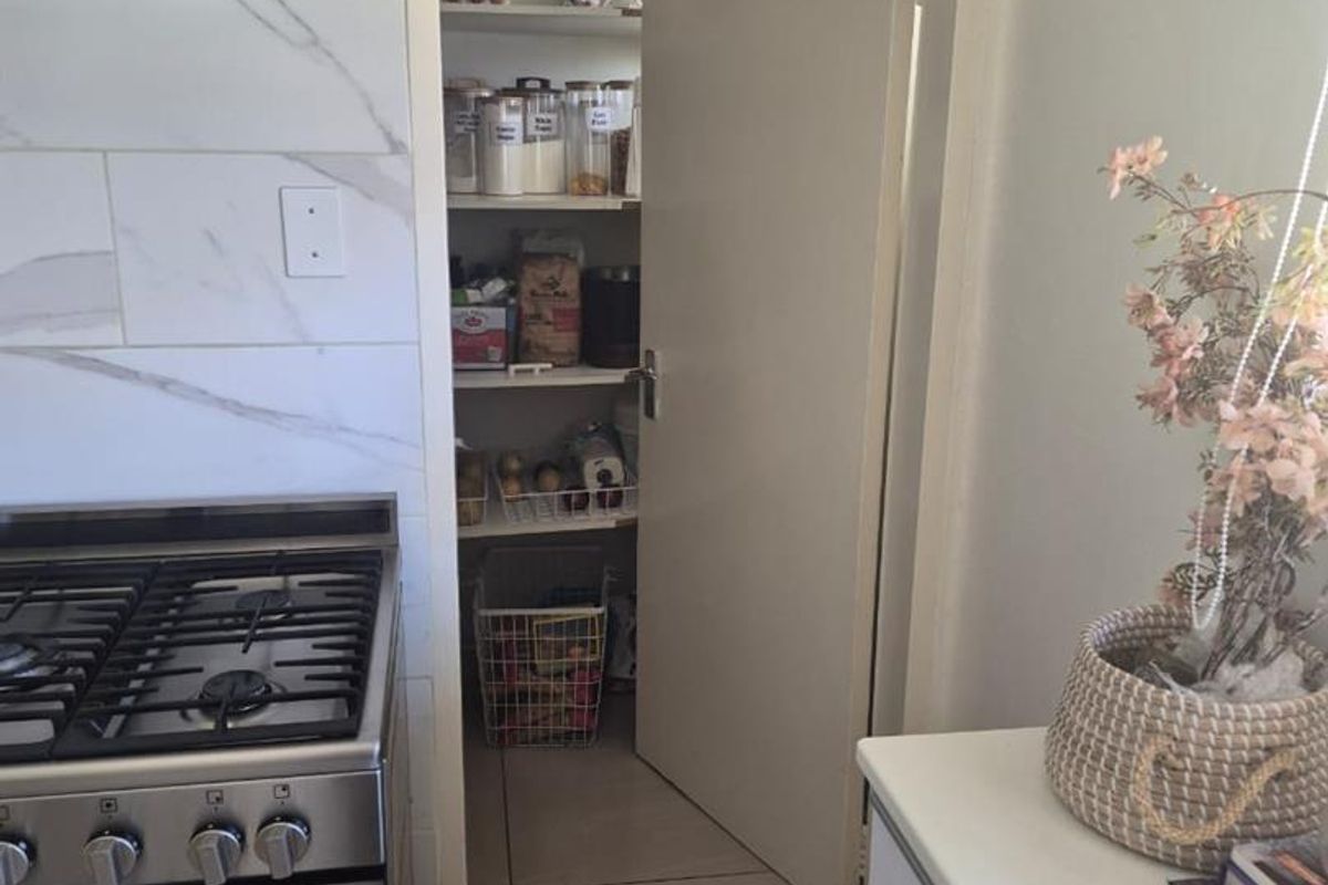 A functional kitchen featuring a stainless steel gas stove, extractor fan, marble-look tiled splashback, and an adjacent walk-in pantry with built-in shelving.