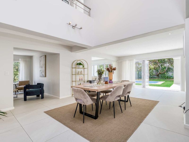 Spacious open-plan dining area featuring high double-volume ceilings, large bi-fold glass doors leading to the garden, and modern tiled flooring.