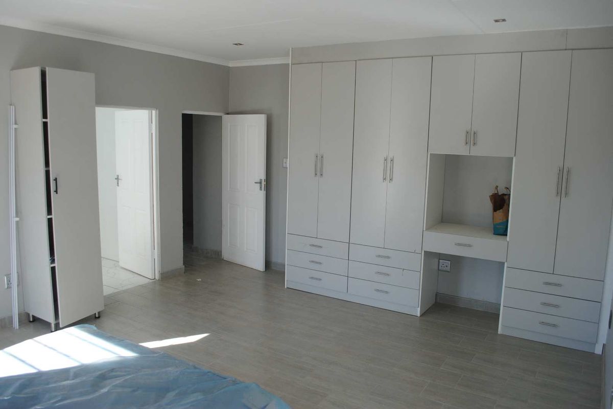 A spacious bedroom featuring light-toned wood-look flooring and extensive built-in cabinetry with integrated desk space.