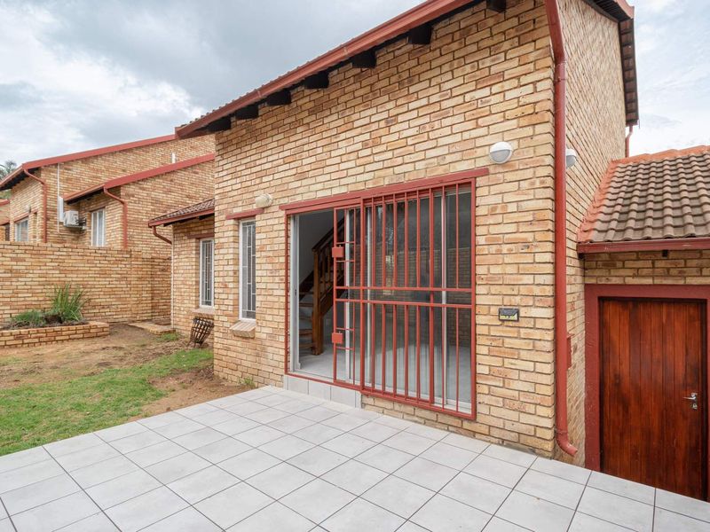Rear view of a face brick townhouse featuring a tiled patio, sliding glass door with security gate, and a separate wooden entrance door.
