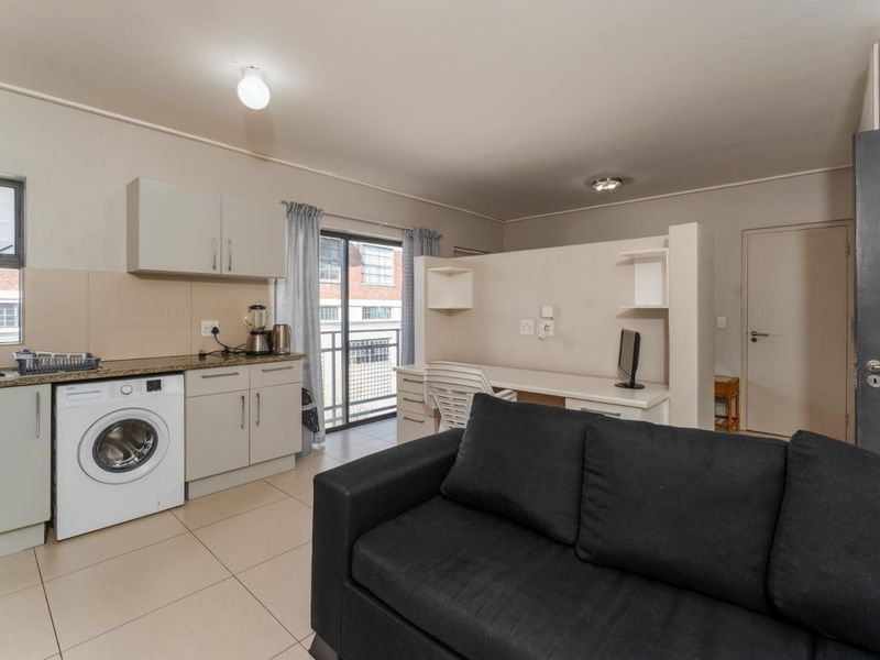 Open-plan apartment living area featuring a compact kitchen with granite countertops, tiled flooring, and a built-in study nook with access to a balcony.