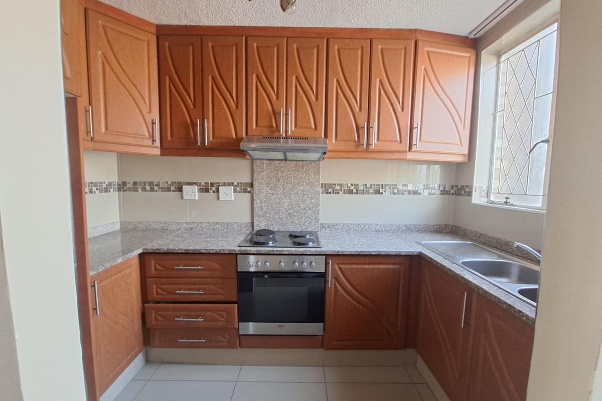 A functional kitchen featuring warm-toned wooden cabinetry, granite countertops, a built-in oven with hob, and a tiled backsplash.