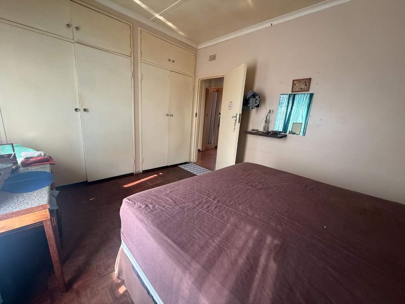 A bedroom featuring built-in cupboards, parquet flooring, and a neutral color palette, offering a functional space with potential for modernization.