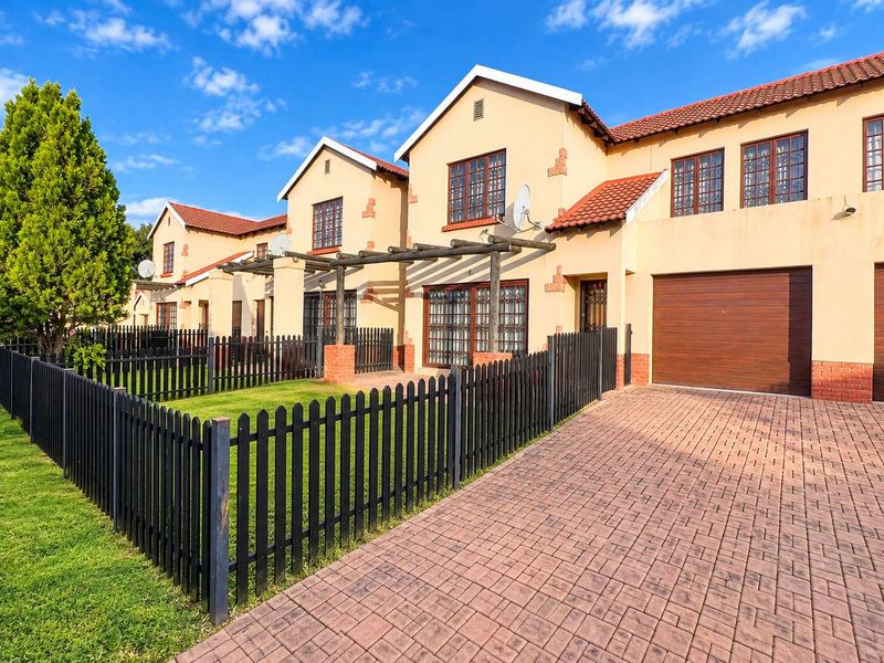 Front elevation of a townhouse complex featuring a paved driveway, private garden with picket fencing, and integrated garage access.