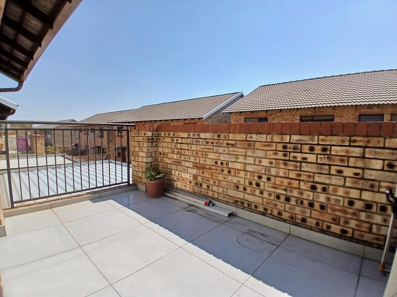 An open-air balcony featuring tiled flooring, a metal safety balustrade, and a face brick boundary wall, offering a clear outdoor space.