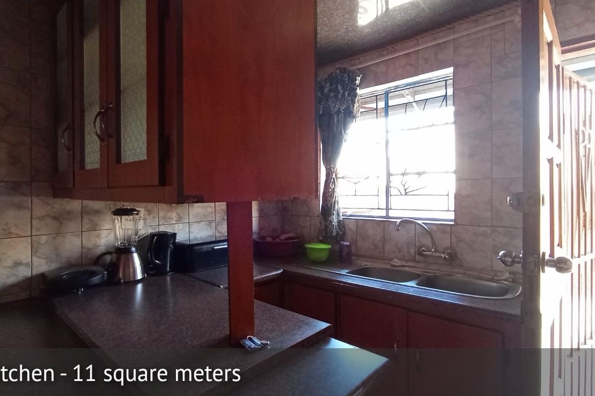 A functional kitchen featuring built-in cabinetry, a double basin sink, and tiled backsplash, with direct access to an exterior security gate.