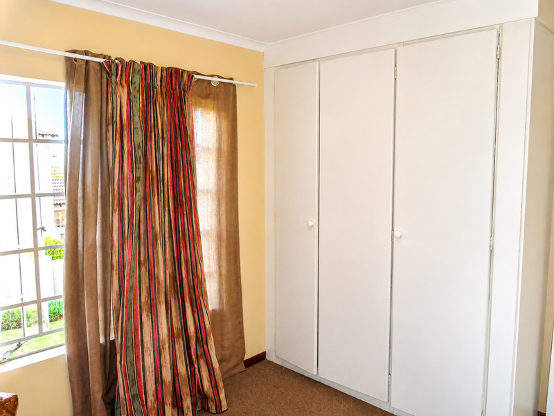 A bedroom featuring built-in cupboards and a grid-pane window, providing a functional space with neutral wall finishes.