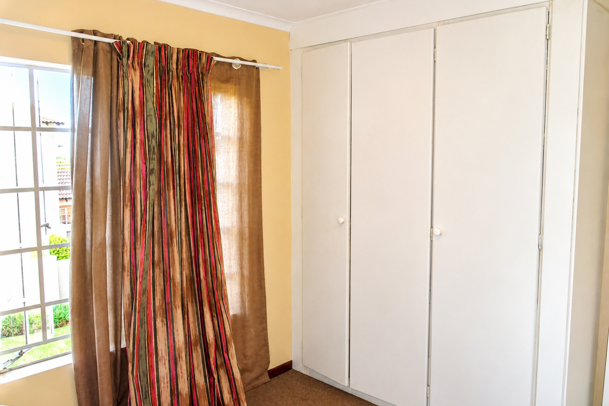 A bedroom featuring built-in cupboards and a grid-pane window, providing a functional space with neutral wall finishes.