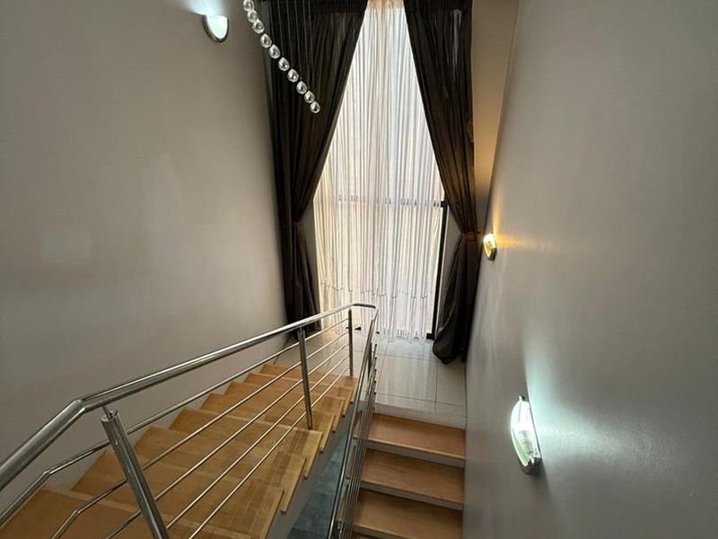 A bright and modern staircase featuring wooden treads, a sleek stainless steel balustrade, and contemporary wall lighting leading to a large window.