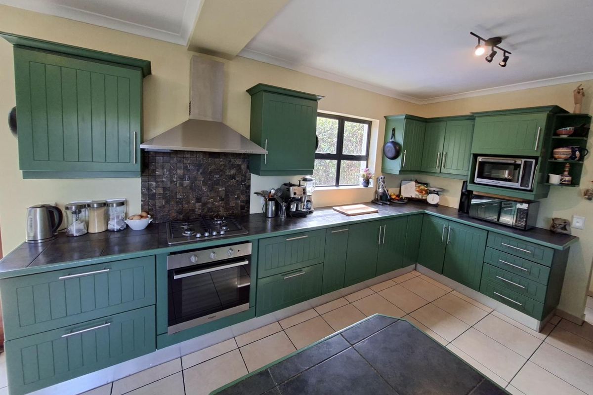 A well-maintained kitchen featuring green shaker-style cabinetry, dark countertops, a gas hob, built-in oven, and tiled flooring.